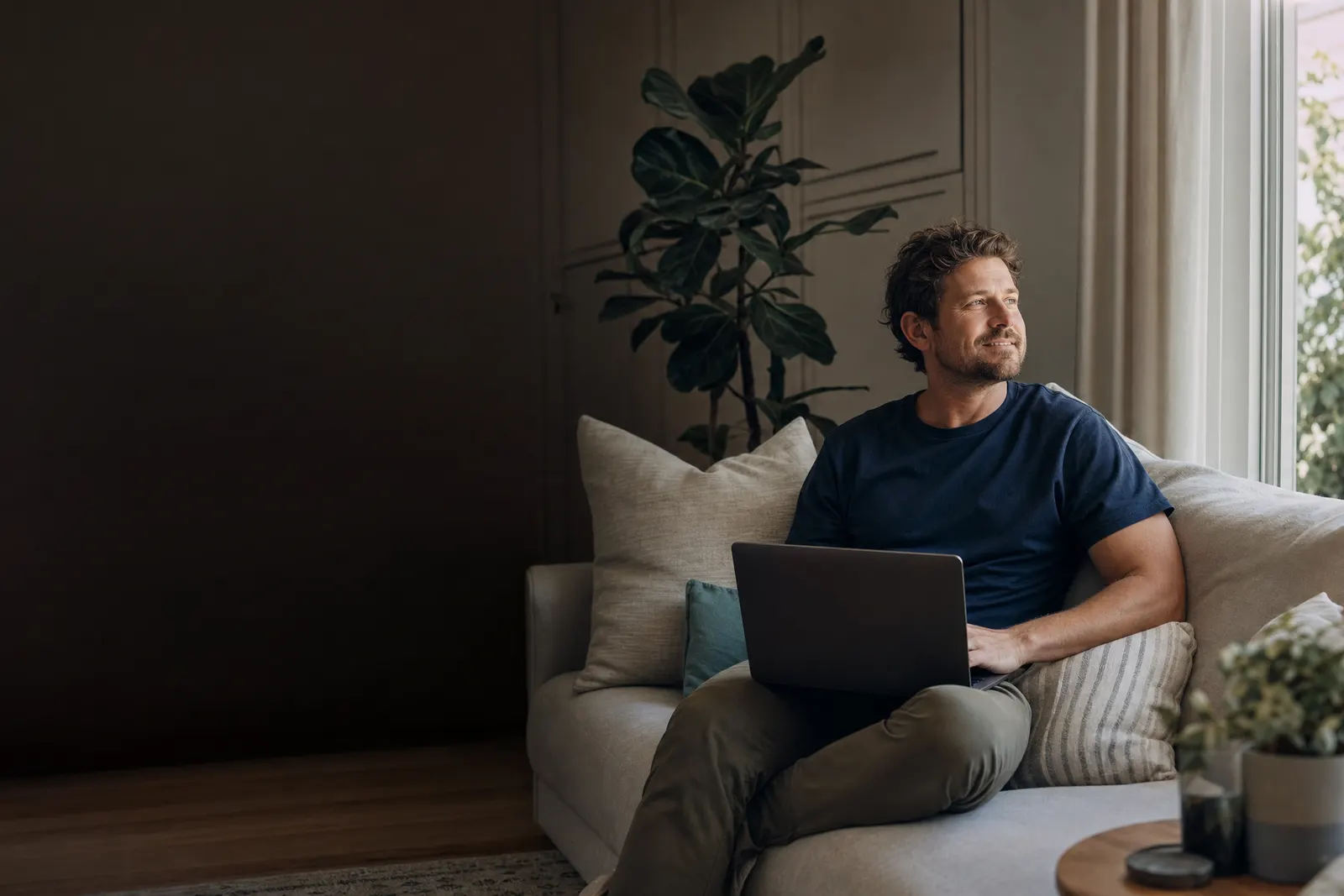 A man relaxing on a sofa at home with a laptop on his knees